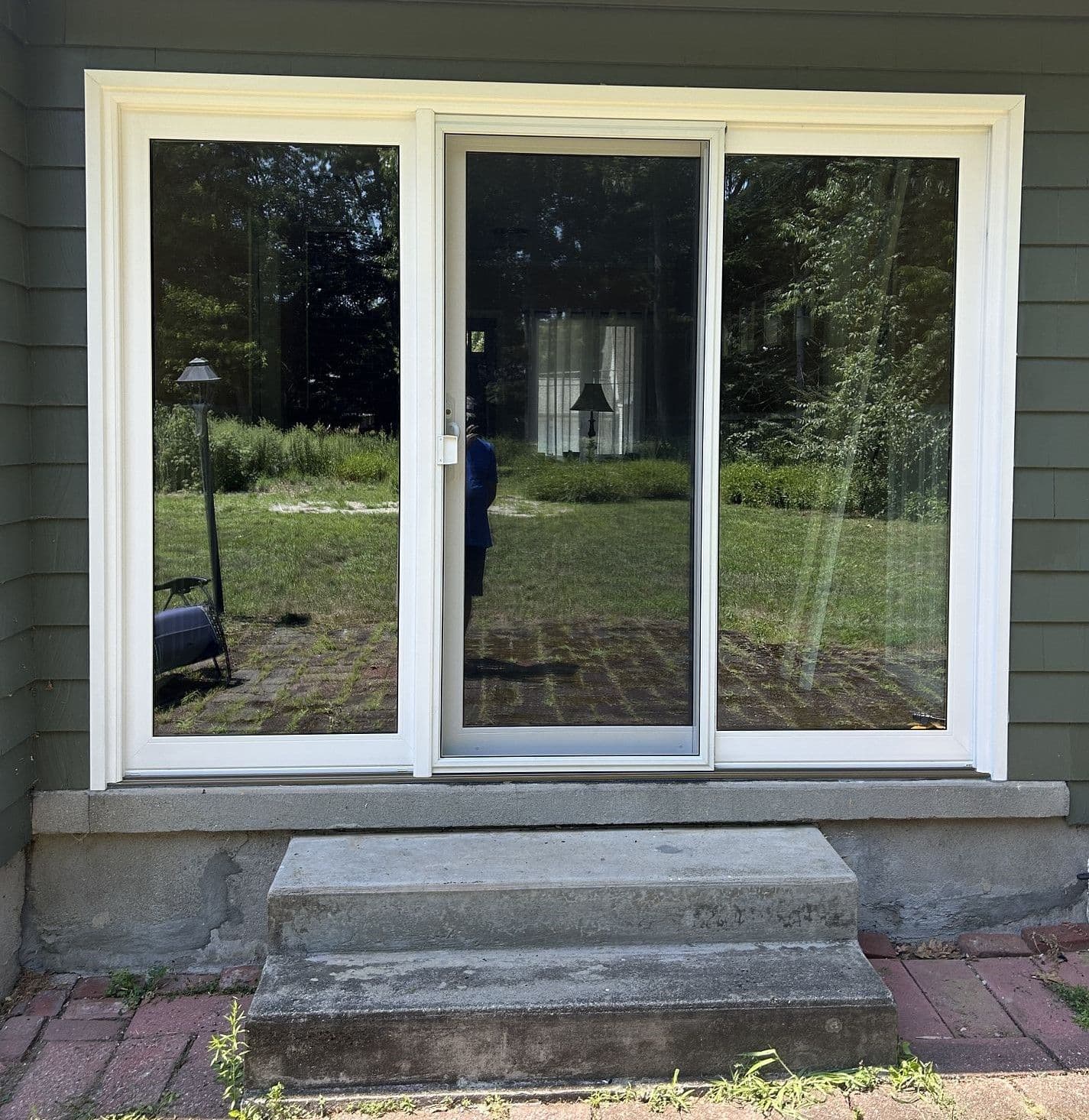 Three newly-installed sliding glass patio doors with white trim on a dark green house.