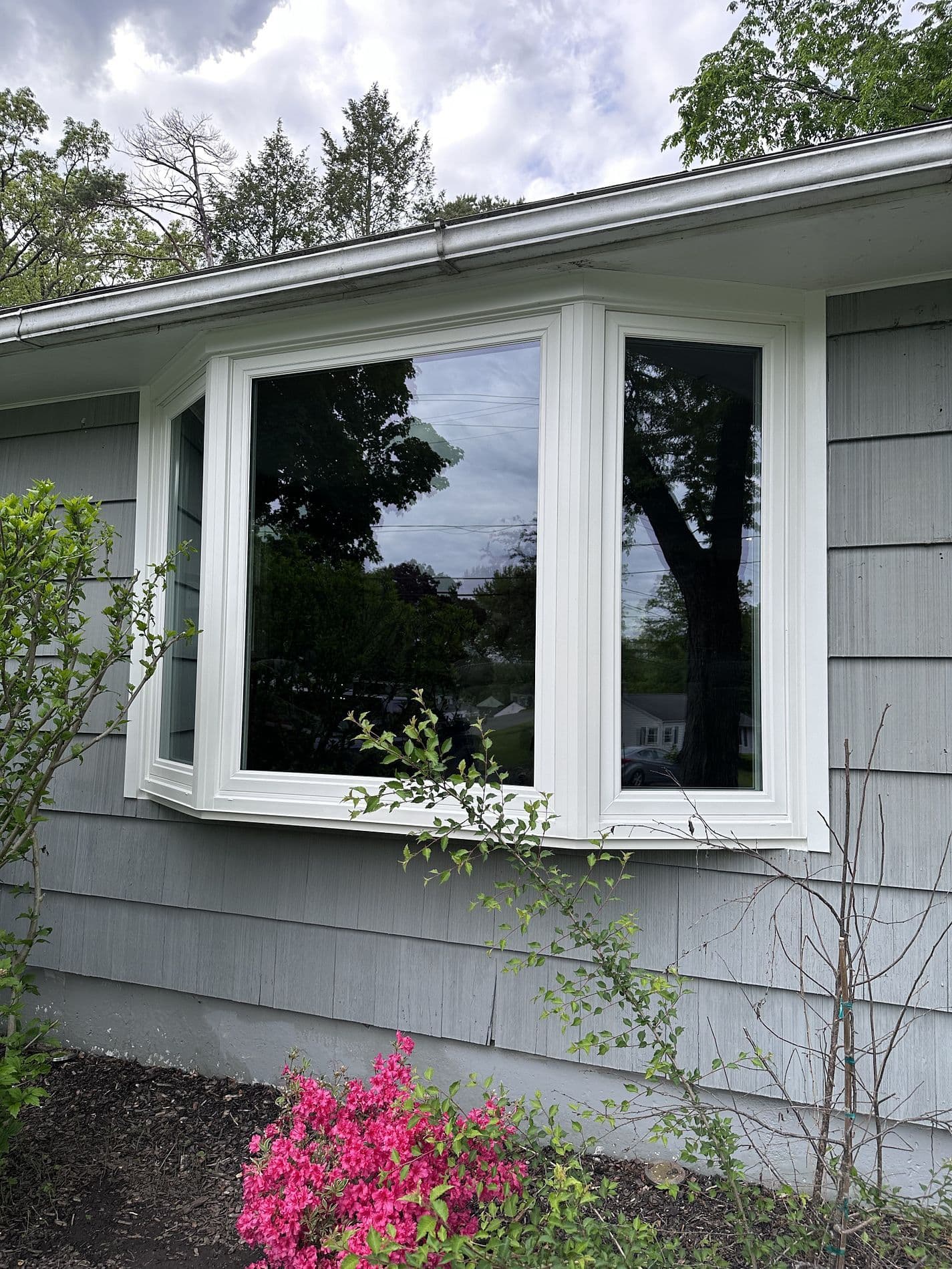 A bay window on a light gray house above a garden.
