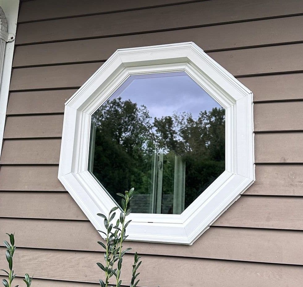 An octagonal window with white trim on a light brown house.