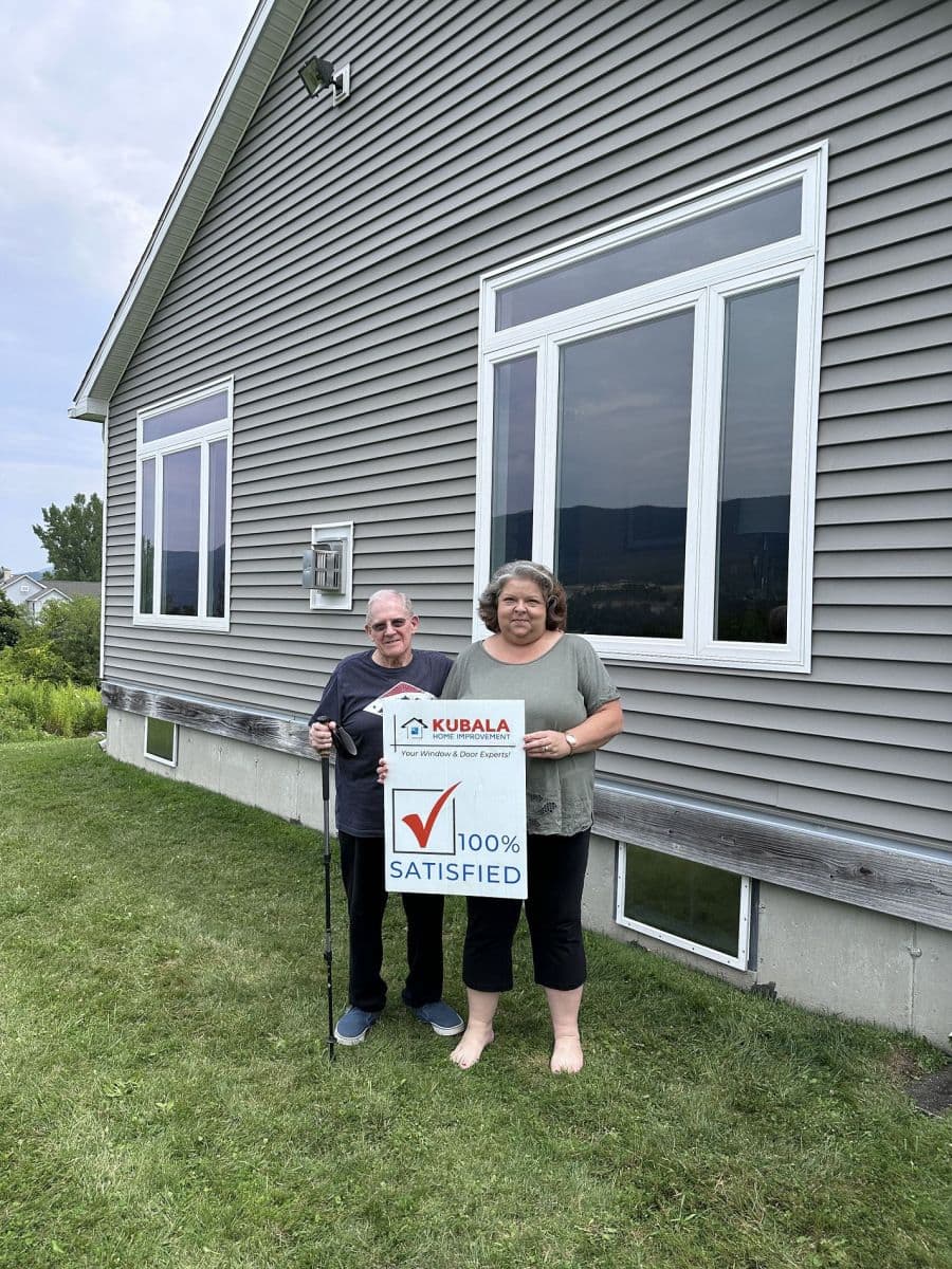 Homeowners hold a sign that reads "100% Satisfied" and stand in front of a newly-installed window.
