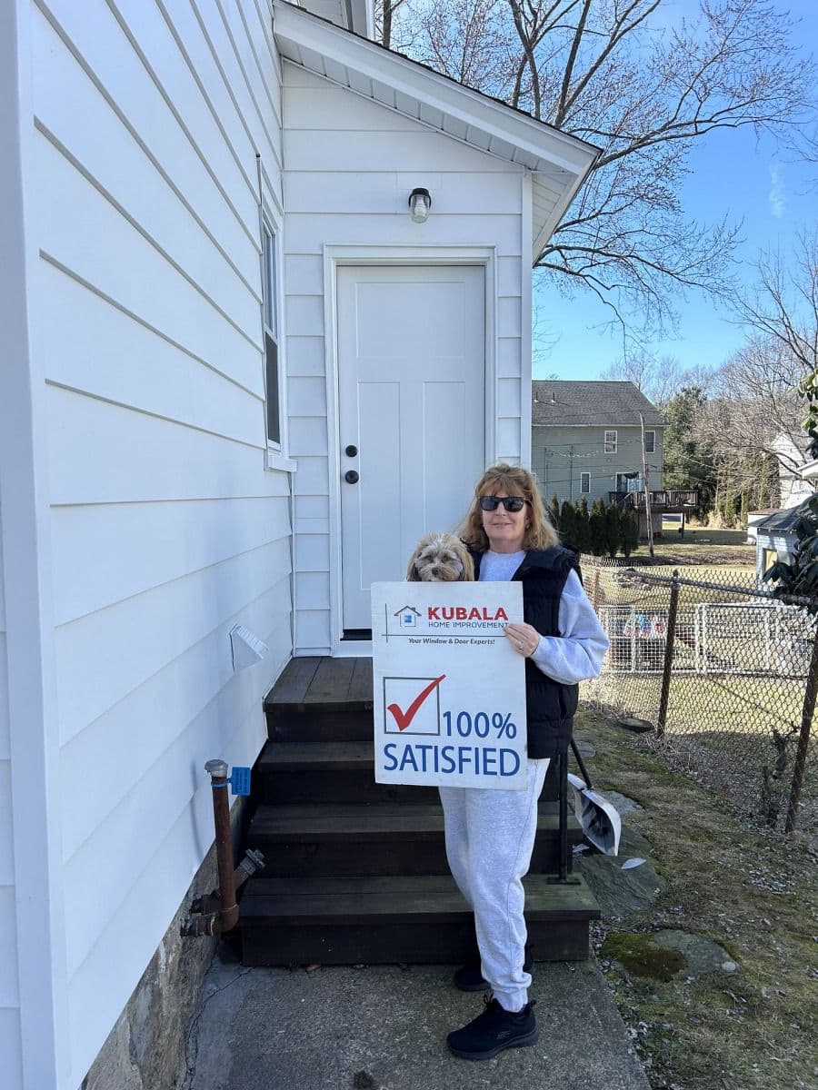 A homeowner holds a sign that reads "100% Satisfied" and stands in front of a new entry door.