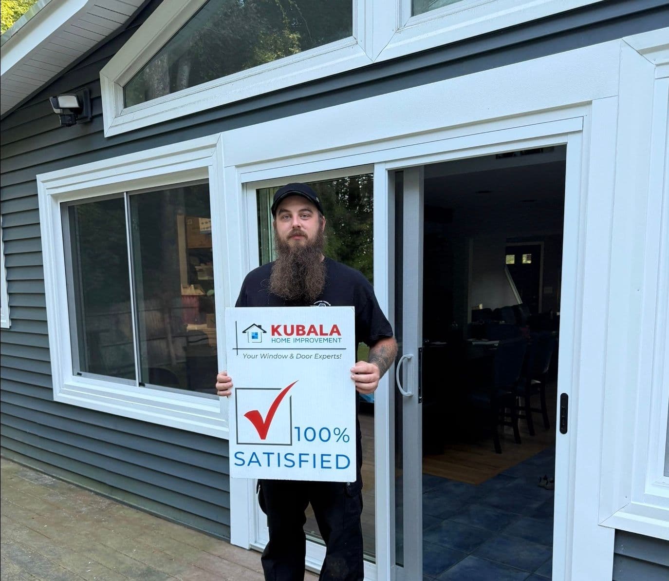 Homeowner holds a sign that reads "100% Satisfied" and stand in front of newly-installed windows.