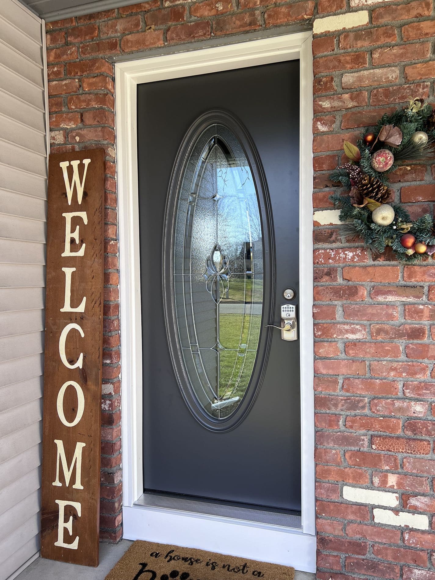 A black entry door with a large glass oval window on a red brick house.