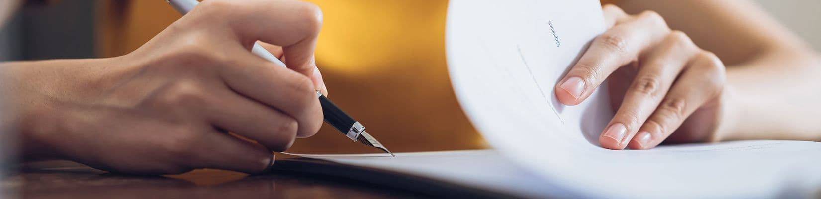 A person holds a pen to sign paperwork.