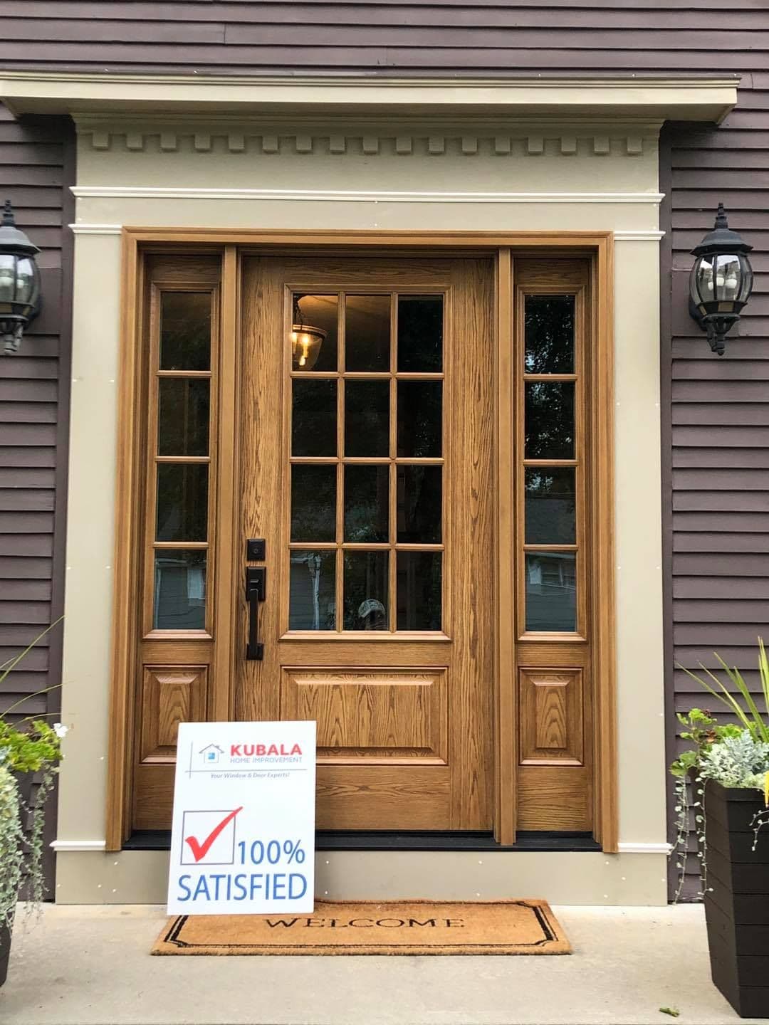 A "100% Satisfied" sign leans agains a medium brown front entry door with light trim on a dark brown house.