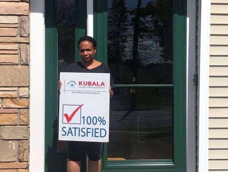 A homeowner holds a sign that reads "100% Satisfied" and stands in front of a new entry door.